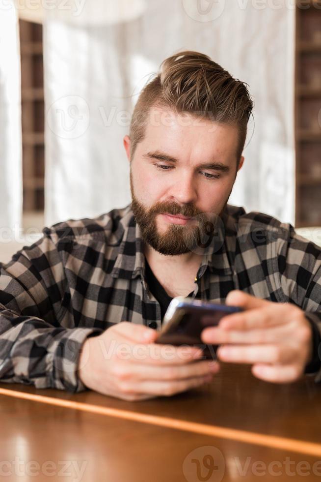 homem sorridente usando smartphone na cafeteria moderna, ele conversando mensagens on-line no celular. redes sociais e conceito da geração do milênio foto