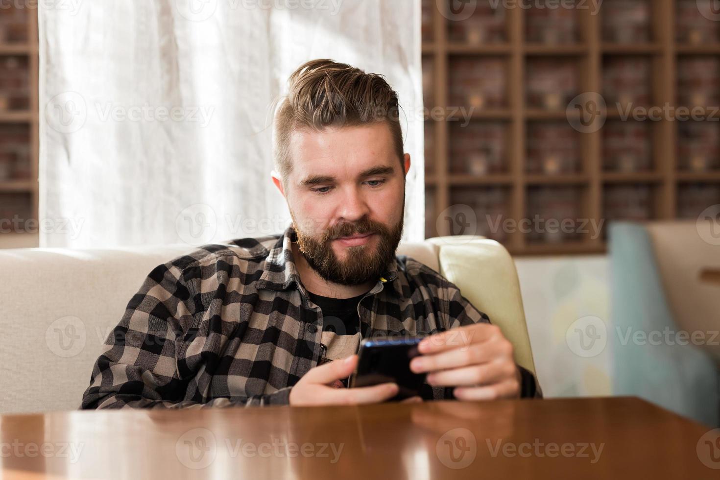 cara jovem hipster procurando notícias de redes sociais lidas via smartphone no tempo livre no café foto