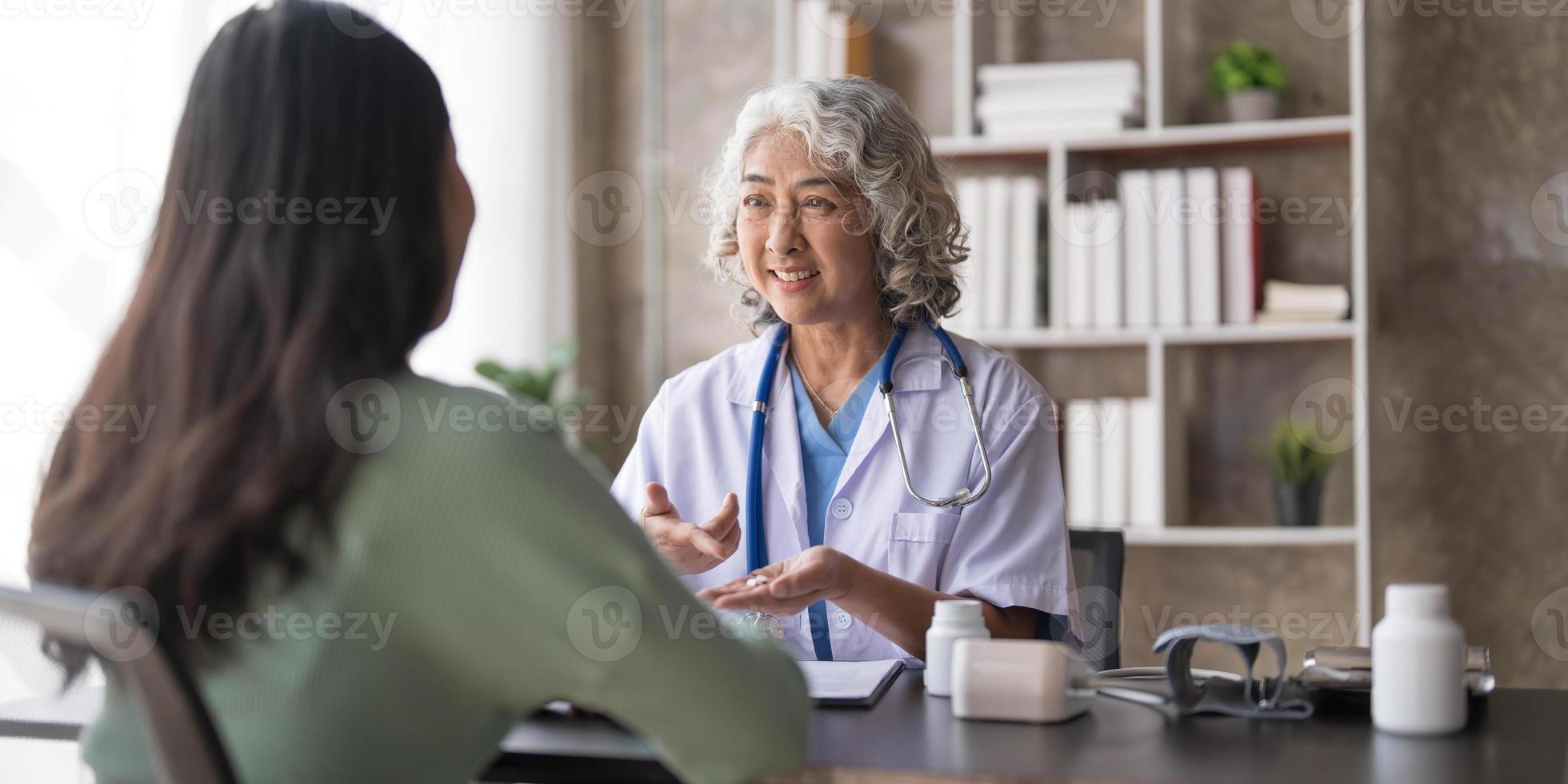 mulher médica sênior está lendo o histórico médico de uma paciente e falando com ela durante a consulta em uma clínica de saúde. médico de jaleco sentado atrás de um laptop no escritório do hospital. foto