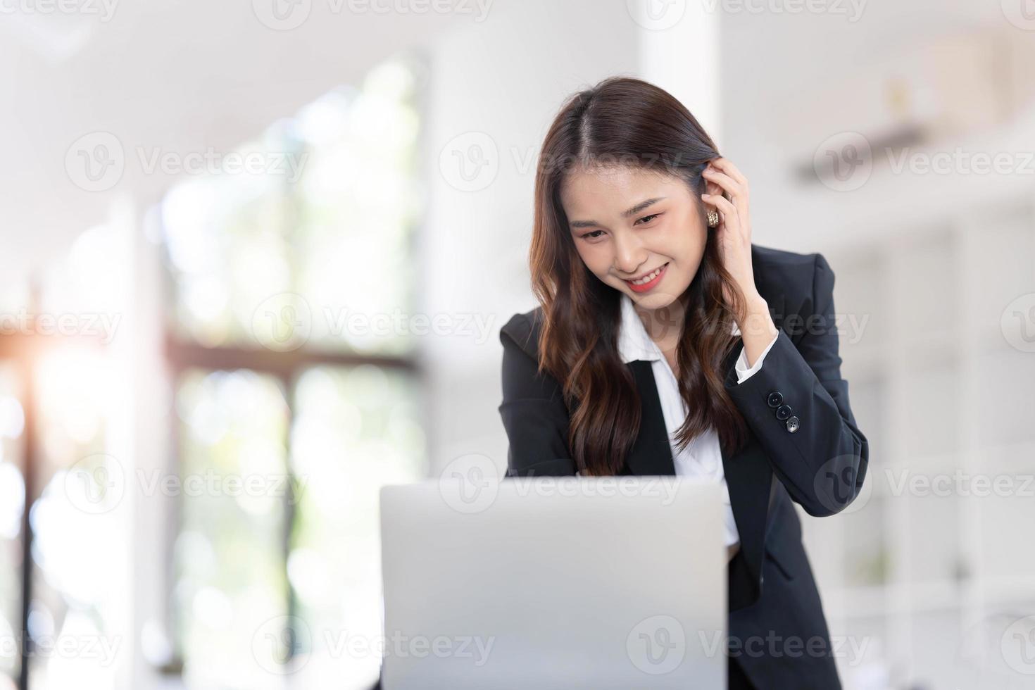 jovem empresária focada em pé na mesa no escritório, usando laptop, olhando para a tela do computador, lendo ou escrevendo e-mail comercial, pesquisando informações na internet, trabalhando no projeto... foto