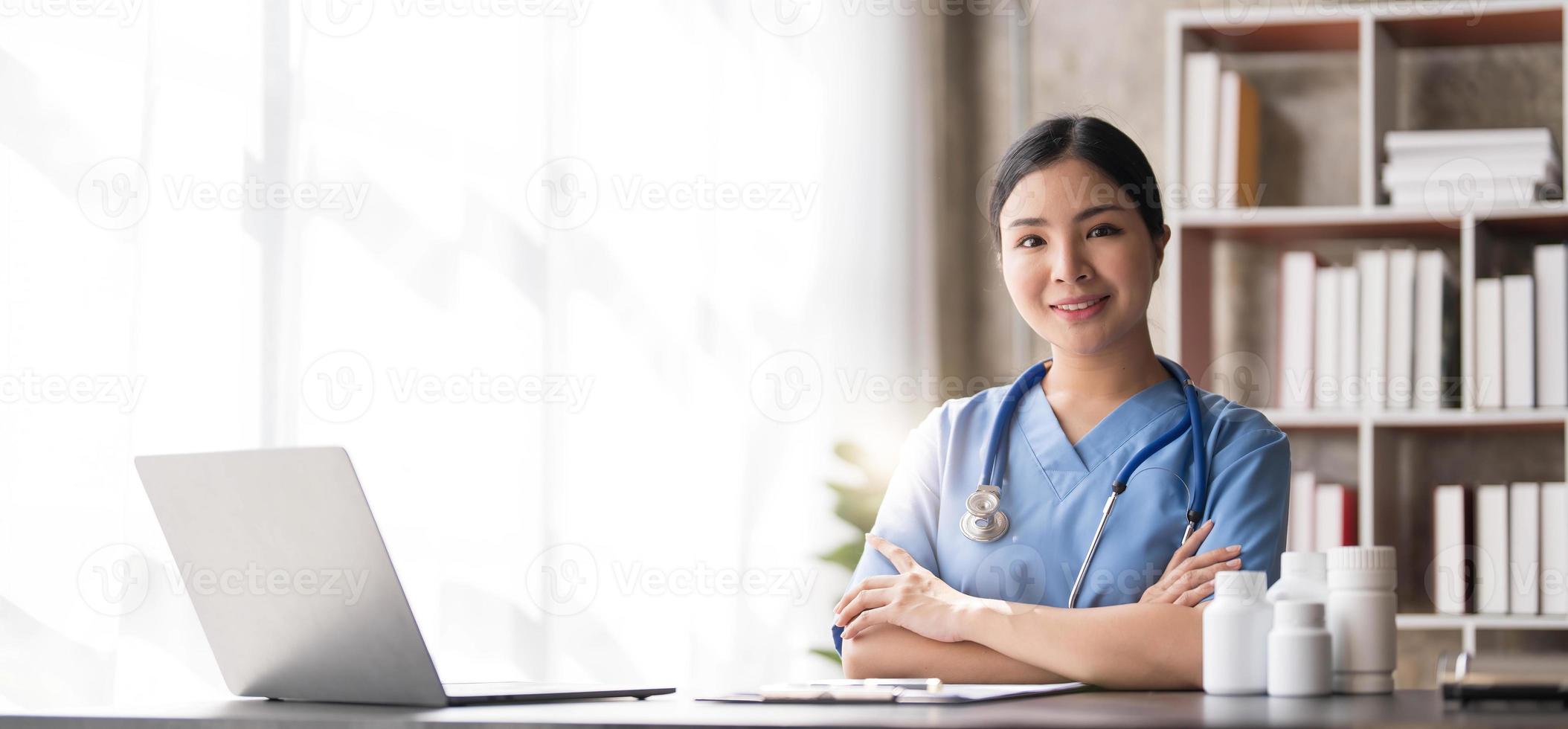 jovem médica asiática bonita sorrindo usando o trabalho com um computador portátil e ela escrevendo algo na papelada ou na prancheta papel branco no escritório da mesa do hospital, conceito médico de saúde foto