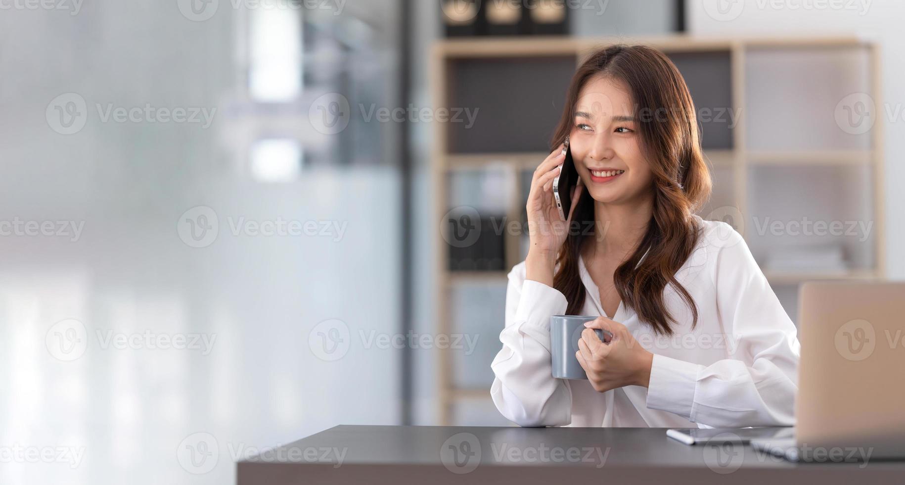jovem empresária asiática senta-se com seu laptop alegremente falando ao telefone com seu cliente explicando os detalhes no escritório. foto