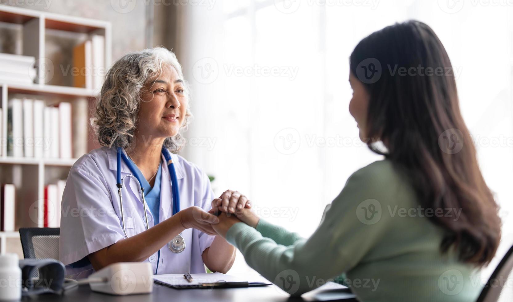 mulher médica sênior está lendo o histórico médico de uma paciente e falando com ela durante a consulta em uma clínica de saúde. médico de jaleco sentado atrás de um laptop no escritório do hospital. foto