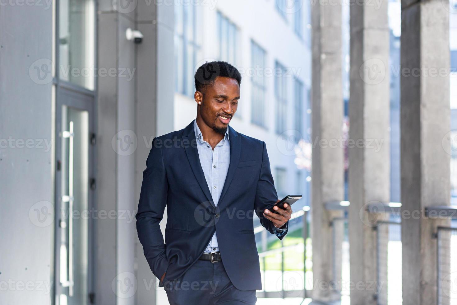 bem sucedido jovem empresário americano africano confiante movendo-se com o celular nas mãos foto