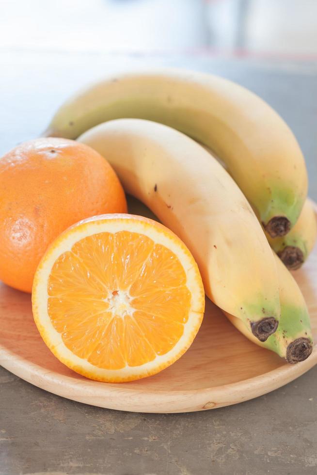 laranjas e bananas em um prato de madeira foto