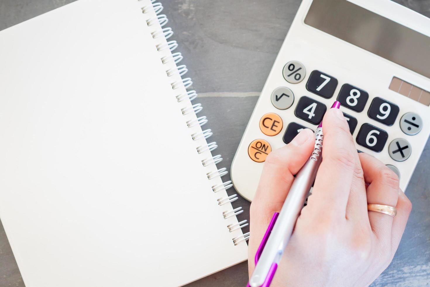 mão segurando uma caneta digitando números em uma calculadora foto