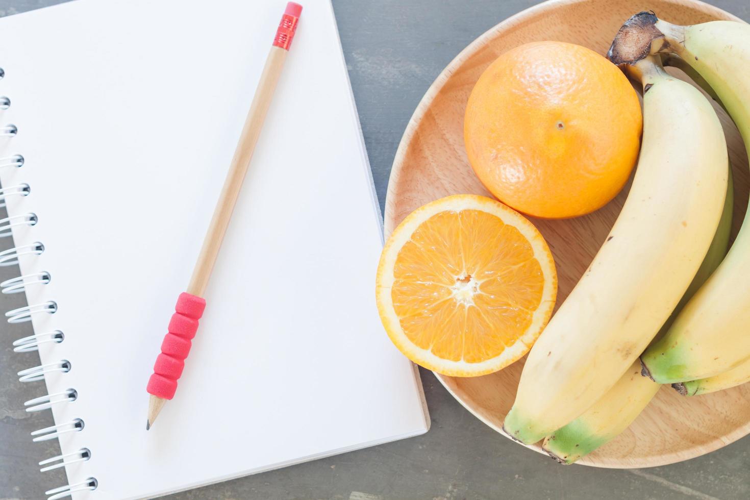 caderno e lápis ao lado de uma tigela de frutas foto