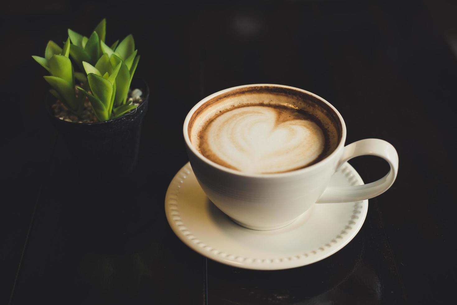 Café com leite em forma de coração com cacto na mesa foto