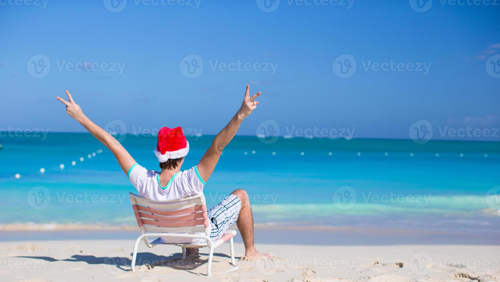 vista traseira do jovem com chapéu de Papai Noel durante as férias na praia foto