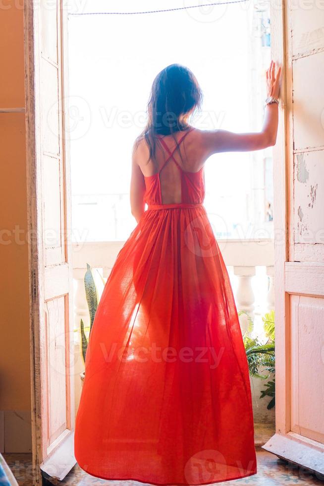 jovem mulher atraente em vestido vermelho na velha varanda em apartamento em havana foto