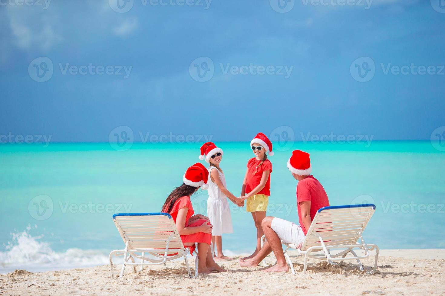 família feliz de quatro pessoas na praia com gorros vermelhos de papai noel foto