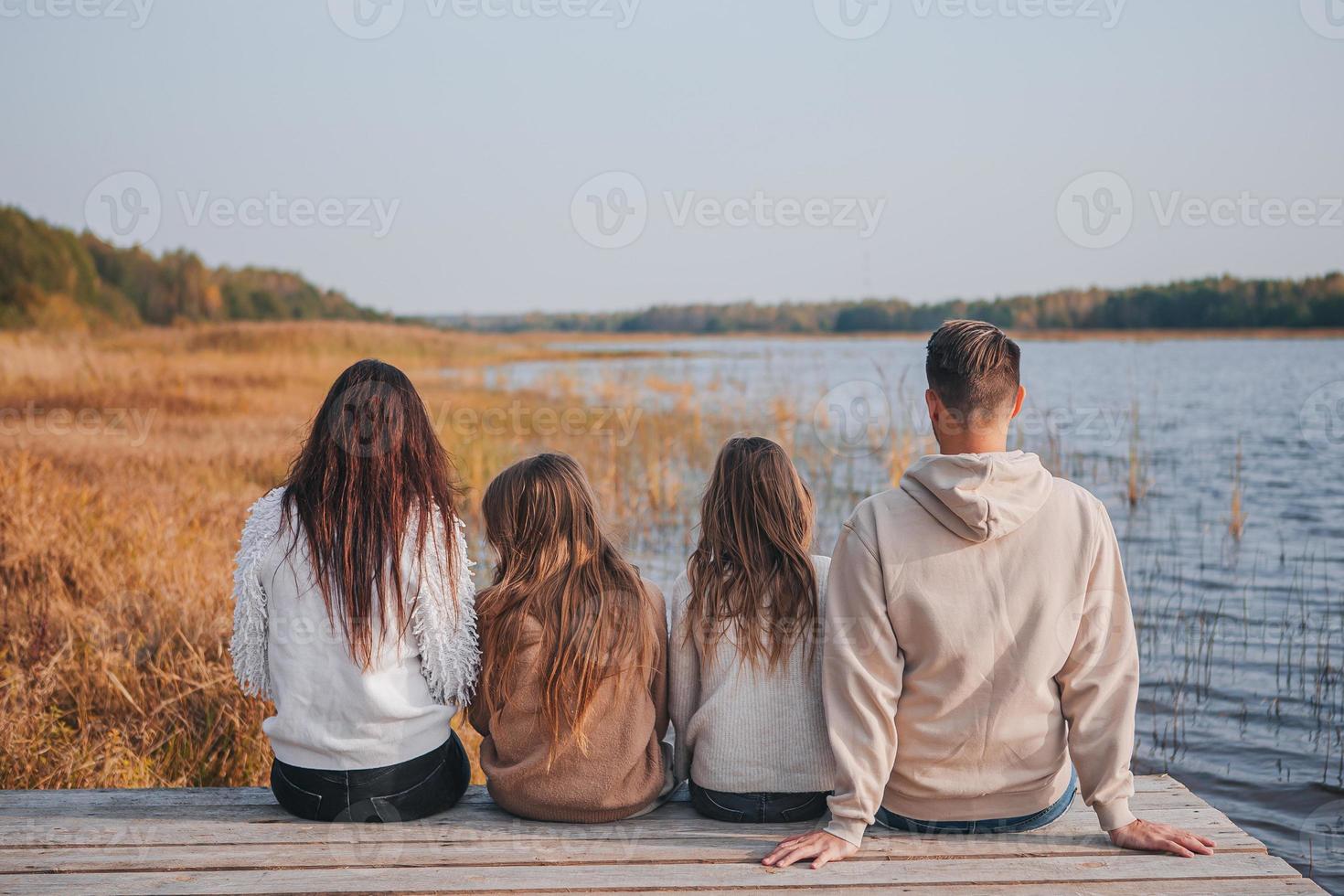 linda família no dia quente de outono perto do lago foto