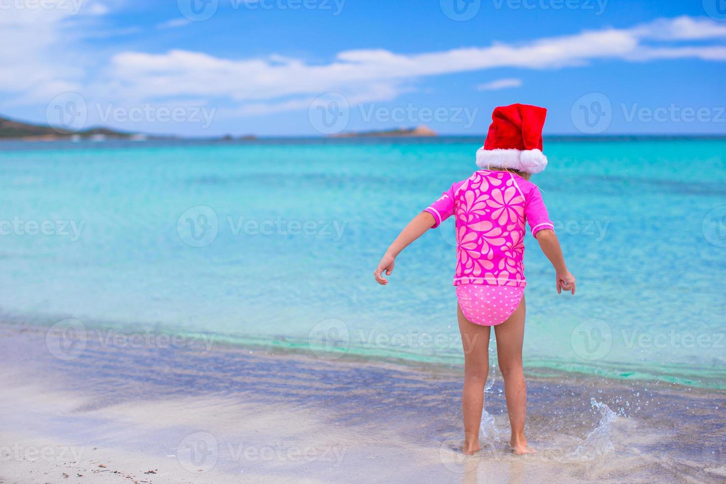 menina adorável com chapéu de Papai Noel vermelho na praia tropical foto