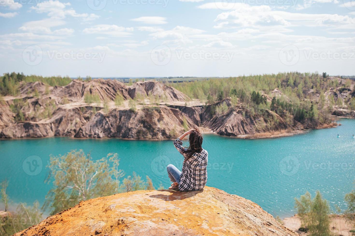 jovem sentada no topo da montagem e se sentindo livre e olhando para o lago azul foto