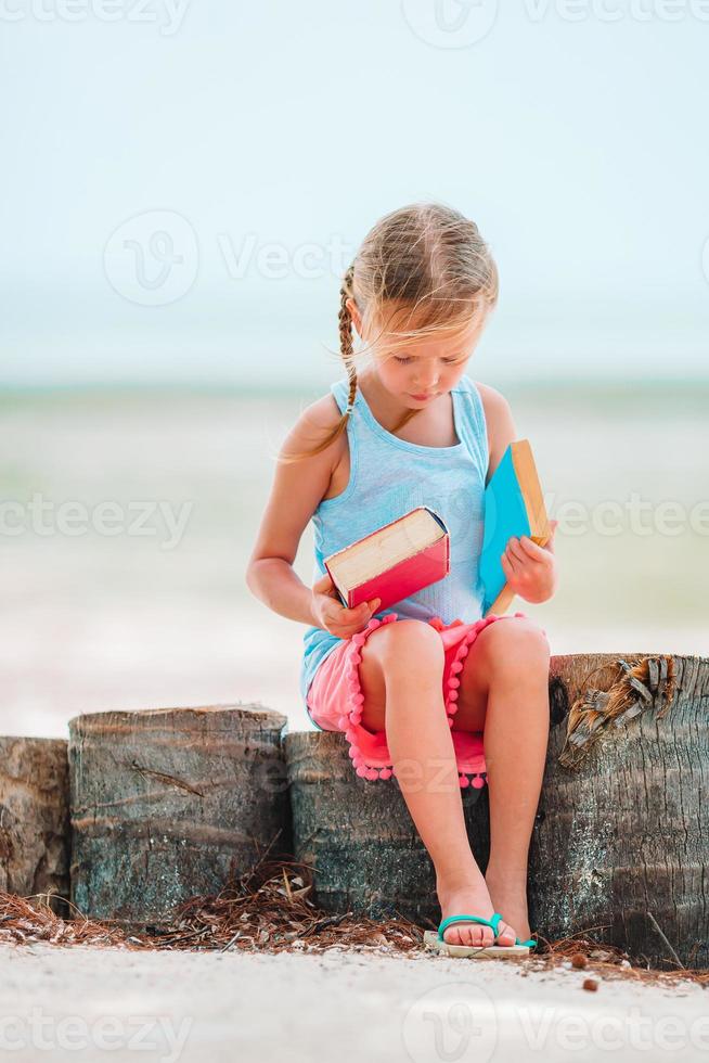 menina adorável lendo livro durante praia branca tropical foto