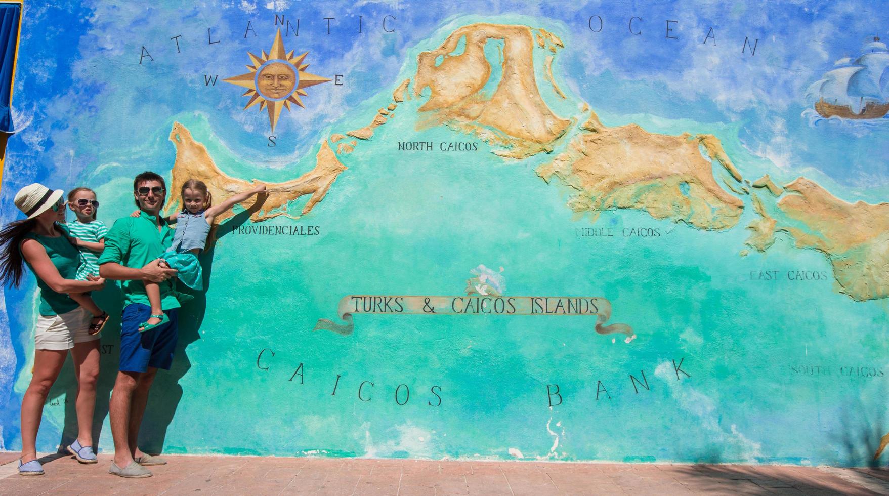família de quatro pessoas perto do grande mapa das ilhas turcas e caicos do caribe pintado na parede foto