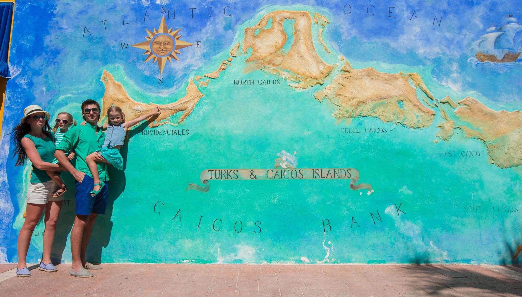 família de quatro pessoas perto do grande mapa das ilhas turcas e caicos do caribe pintado na parede foto