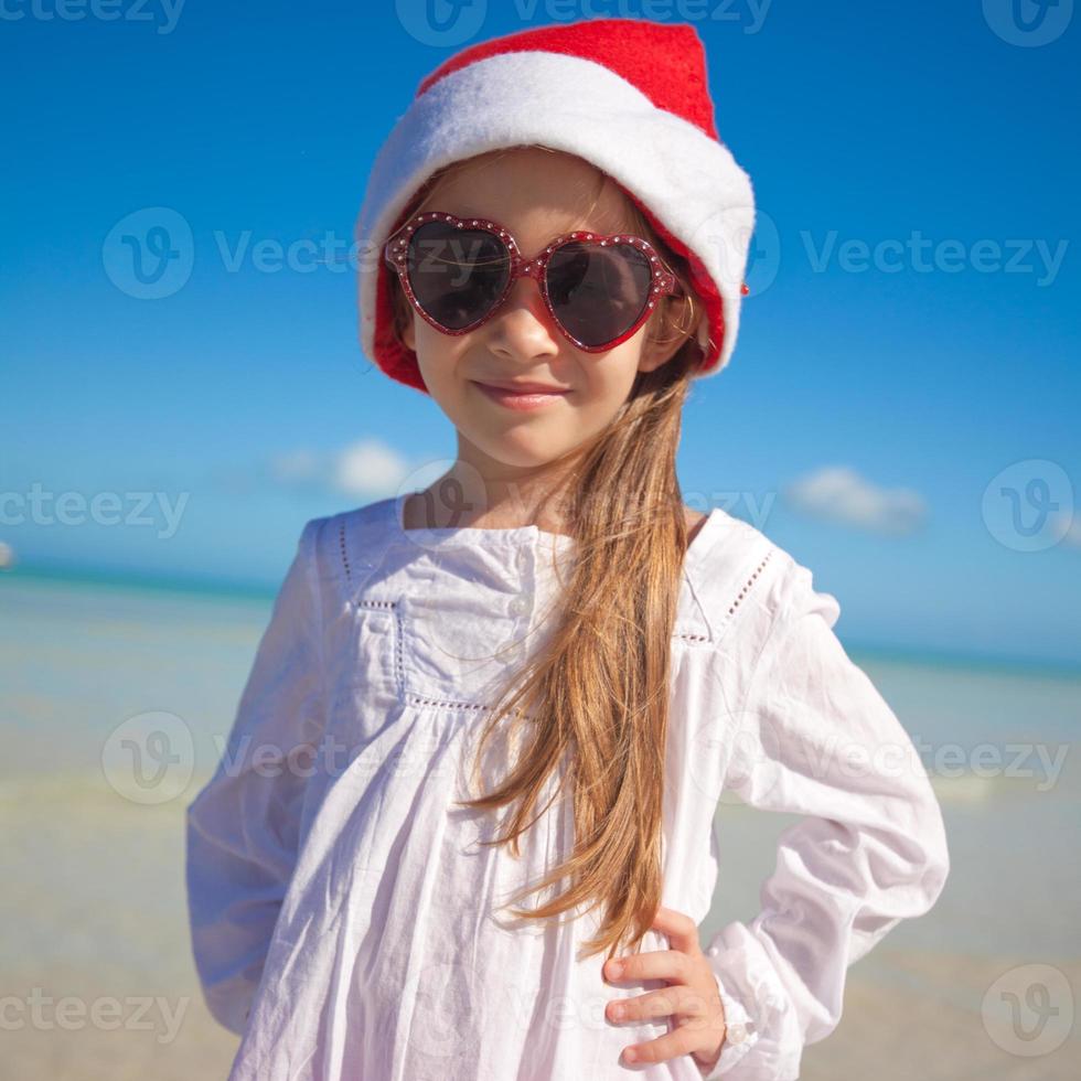 menina adorável com chapéu de Papai Noel vermelho na praia tropical foto