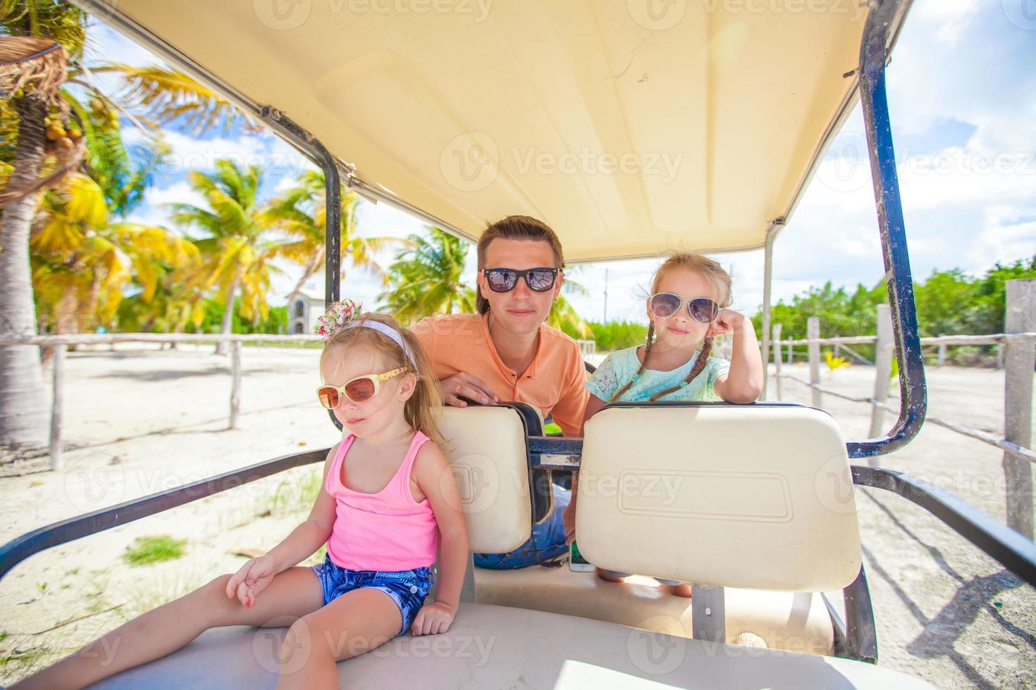 pai e suas filhas dirigindo carrinho de golfe na praia tropical foto