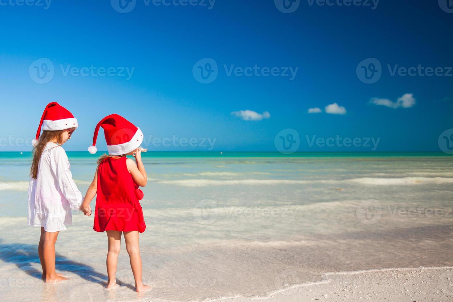 meninas adoráveis em chapéus de Papai Noel durante as férias na praia foto
