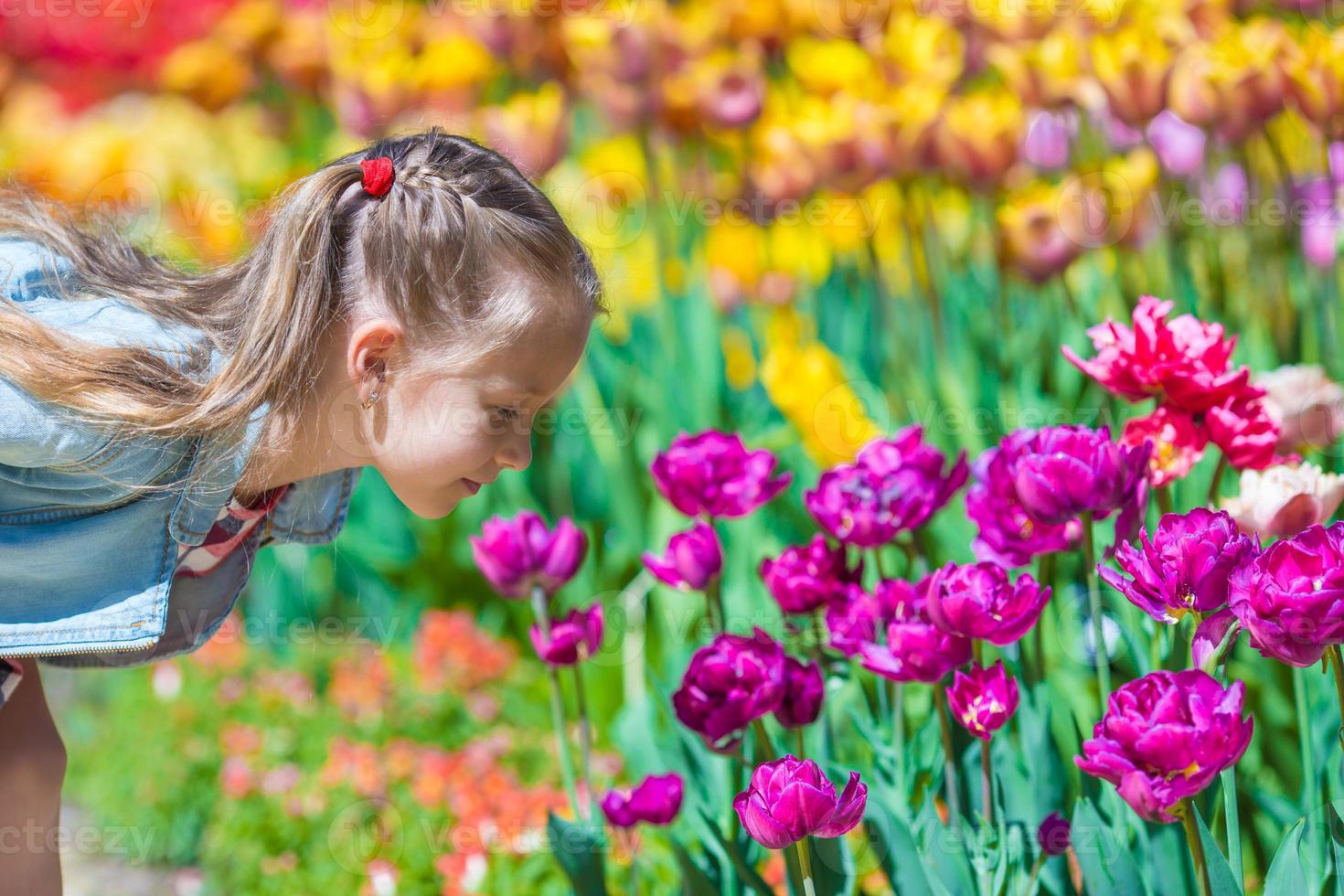 menina adorável cheirando tulipas coloridas no dia de verão foto