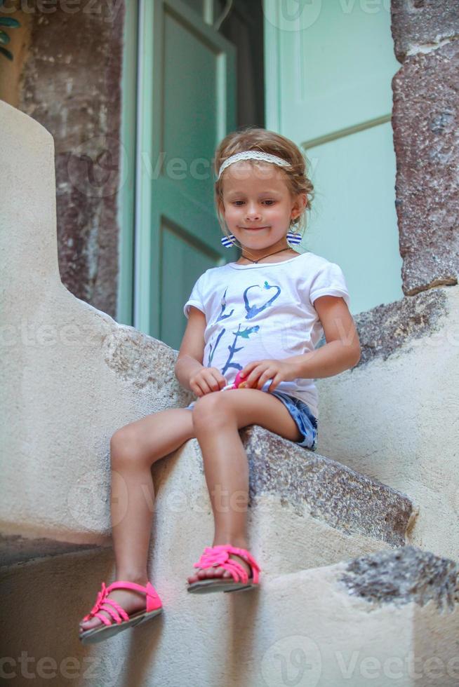 adorável menina sentada nos degraus da velha casa na vila de emporio, santorini, grécia foto