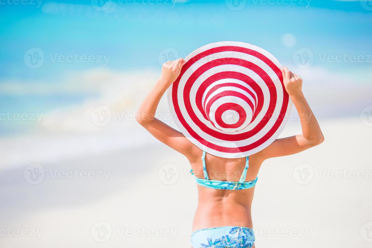 adorável menina com grande chapéu vermelho caminhando ao longo da praia de areia branca do Caribe foto