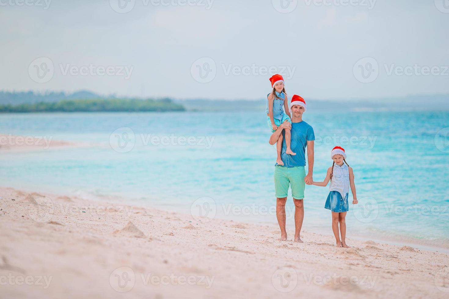 família feliz em chapéus de papai noel vermelhos em uma praia tropical comemorando as férias de natal foto