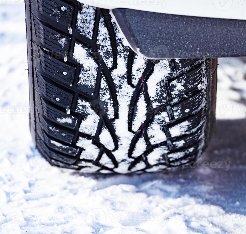 tiro de close-up de pneu cravejado de automóvel coberto de neve na estrada de neve de inverno foto