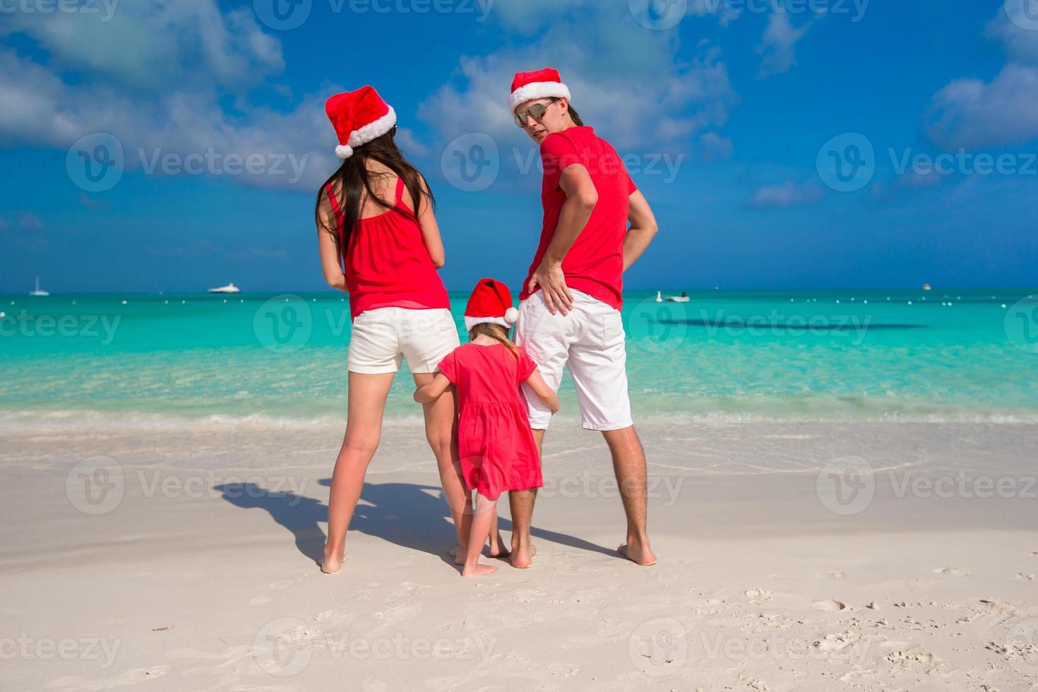 família feliz de três em chapéus de natal durante as férias tropicais foto