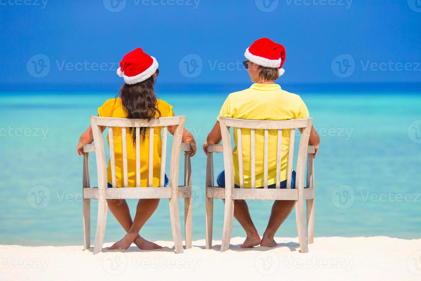 jovem casal de chapéu de papai noel relaxando na praia tropical durante as férias de natal foto