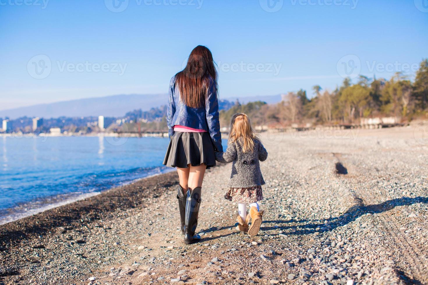 menina e sua mãe caminhando na praia em dia ensolarado de inverno foto