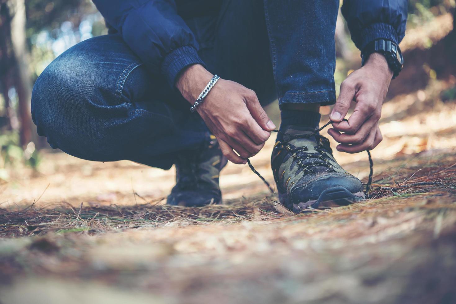 jovem caminhante amarra os cadarços de seu sapato enquanto mochila na floresta foto