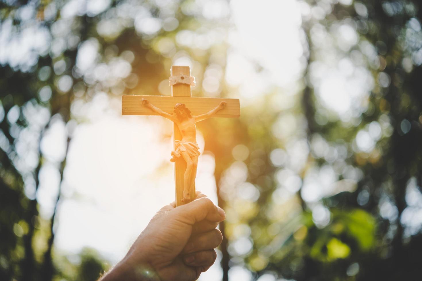 mãos segurando uma cruz de madeira sobre o céu foto