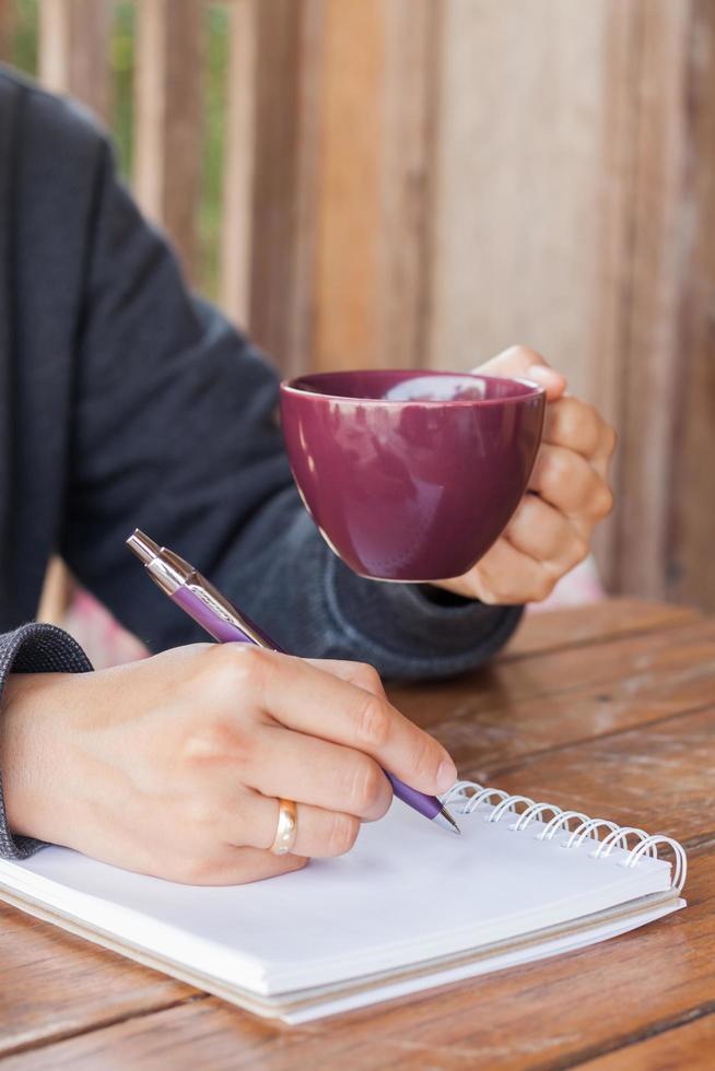 pessoa segurando uma xícara de café roxa e escrevendo foto