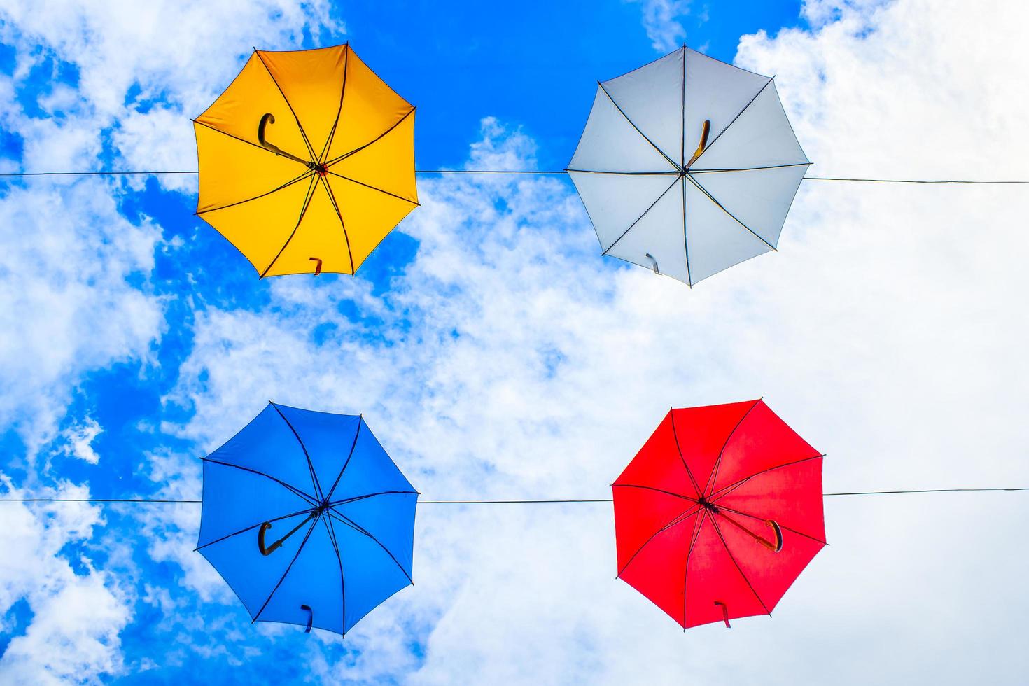 quatro guarda-chuvas de cores variadas pendurados em cabos sob céu nublado foto