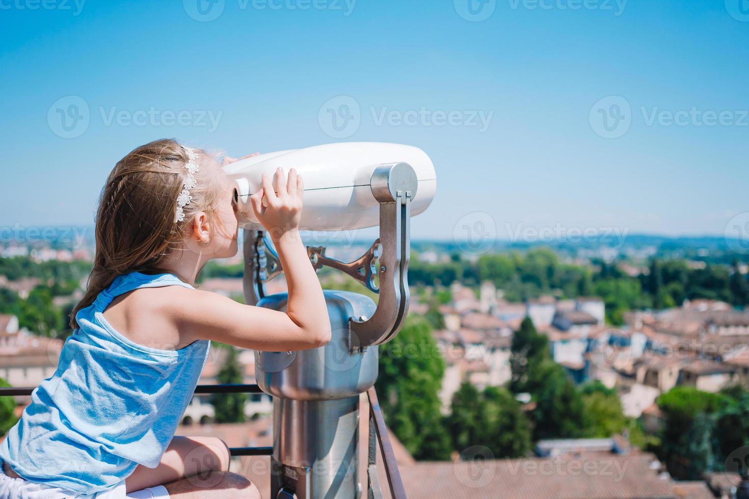 linda garota olhando binóculo operado por moedas no terraço em uma pequena cidade na toscana foto
