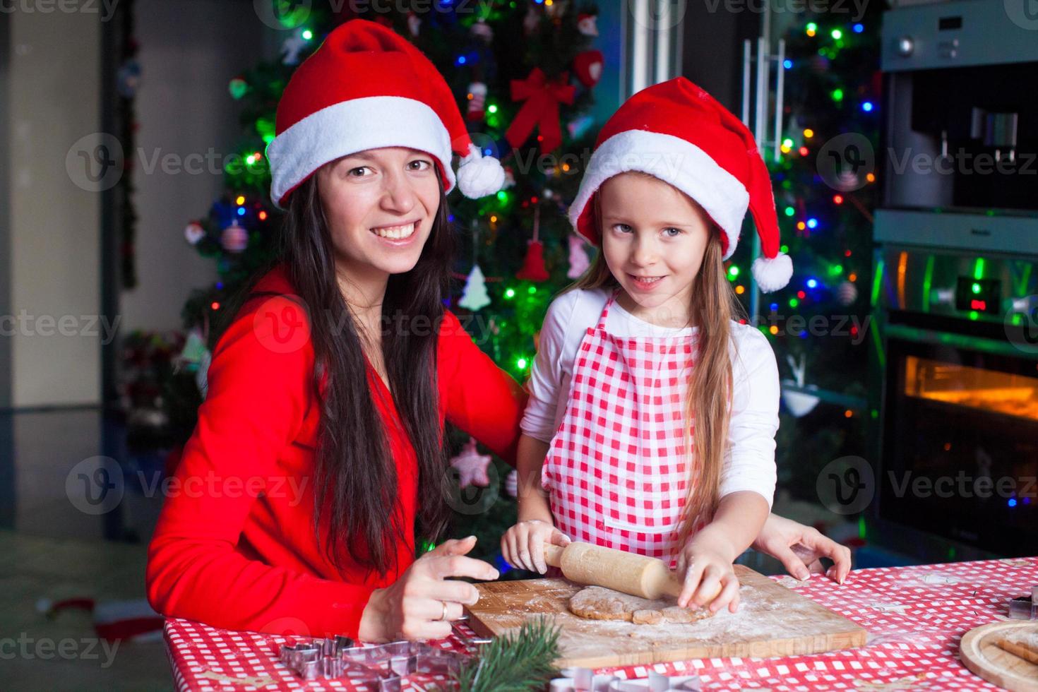 família feliz em chapéus de papai noel assando biscoitos de gengibre de natal juntos foto