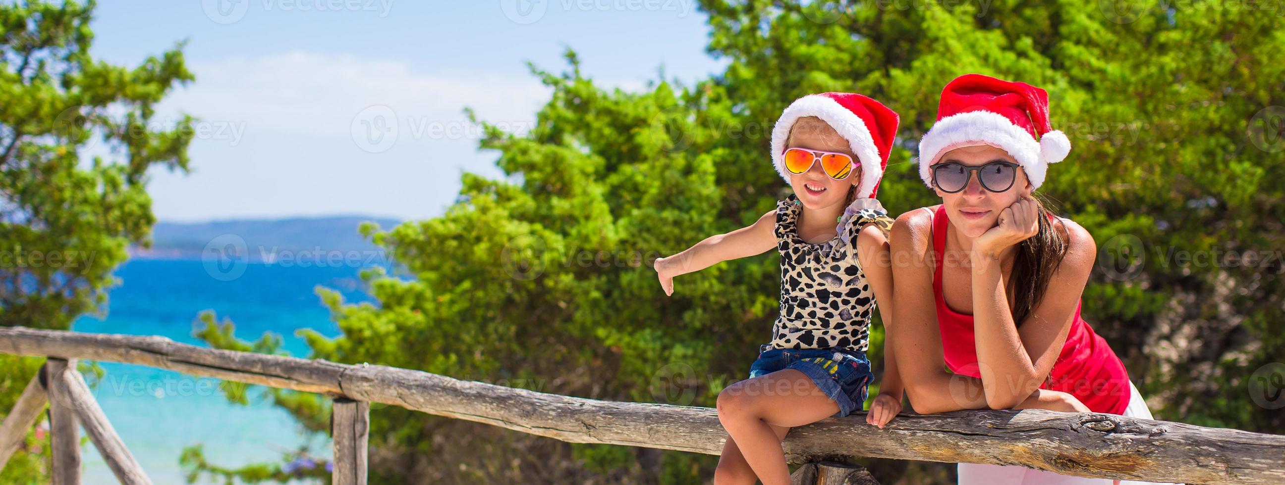 jovem mãe e filha com chapéu vermelho de natal na praia tropical foto