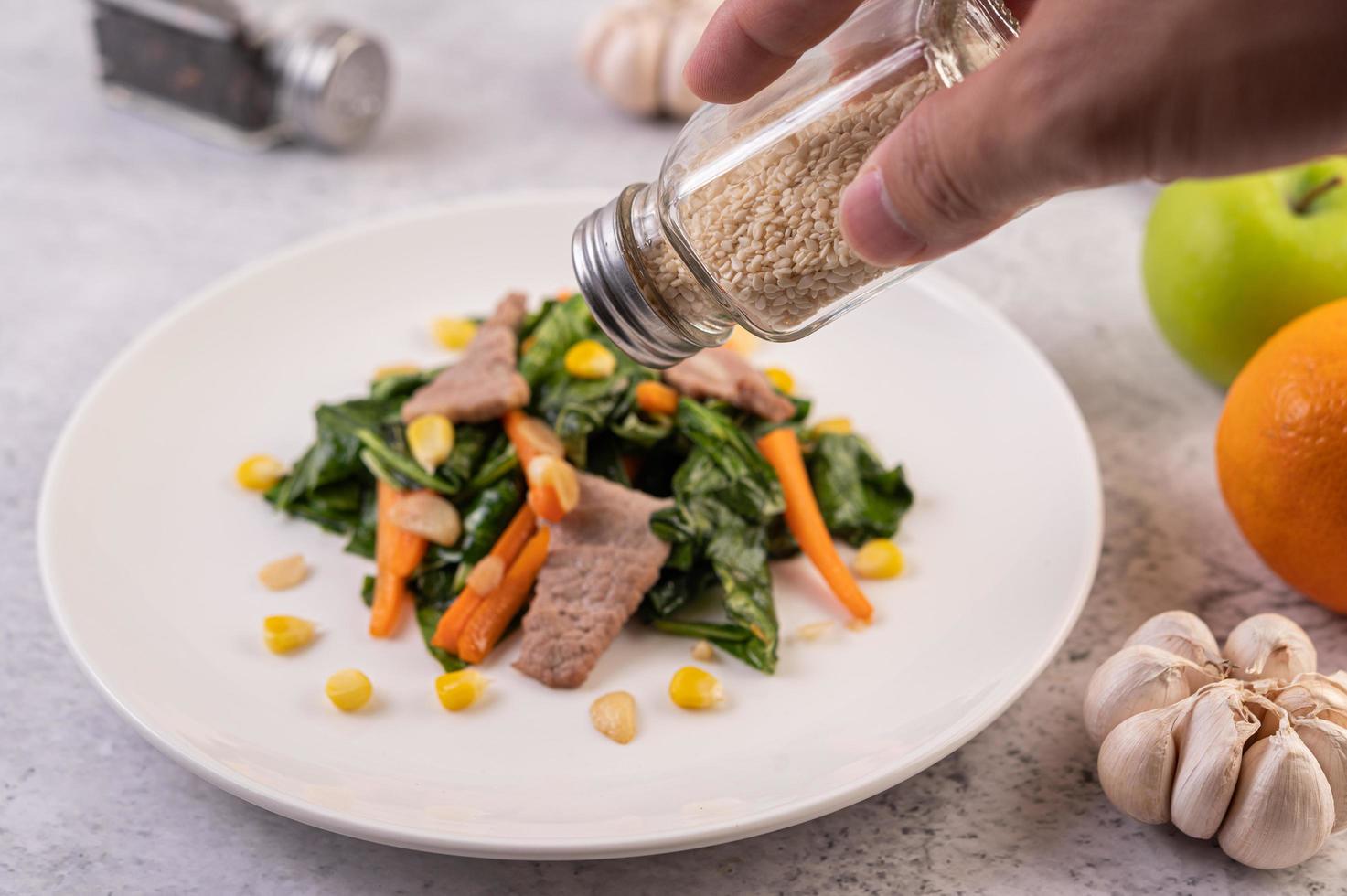 mão derramando sementes de gergelim em um prato de comida foto