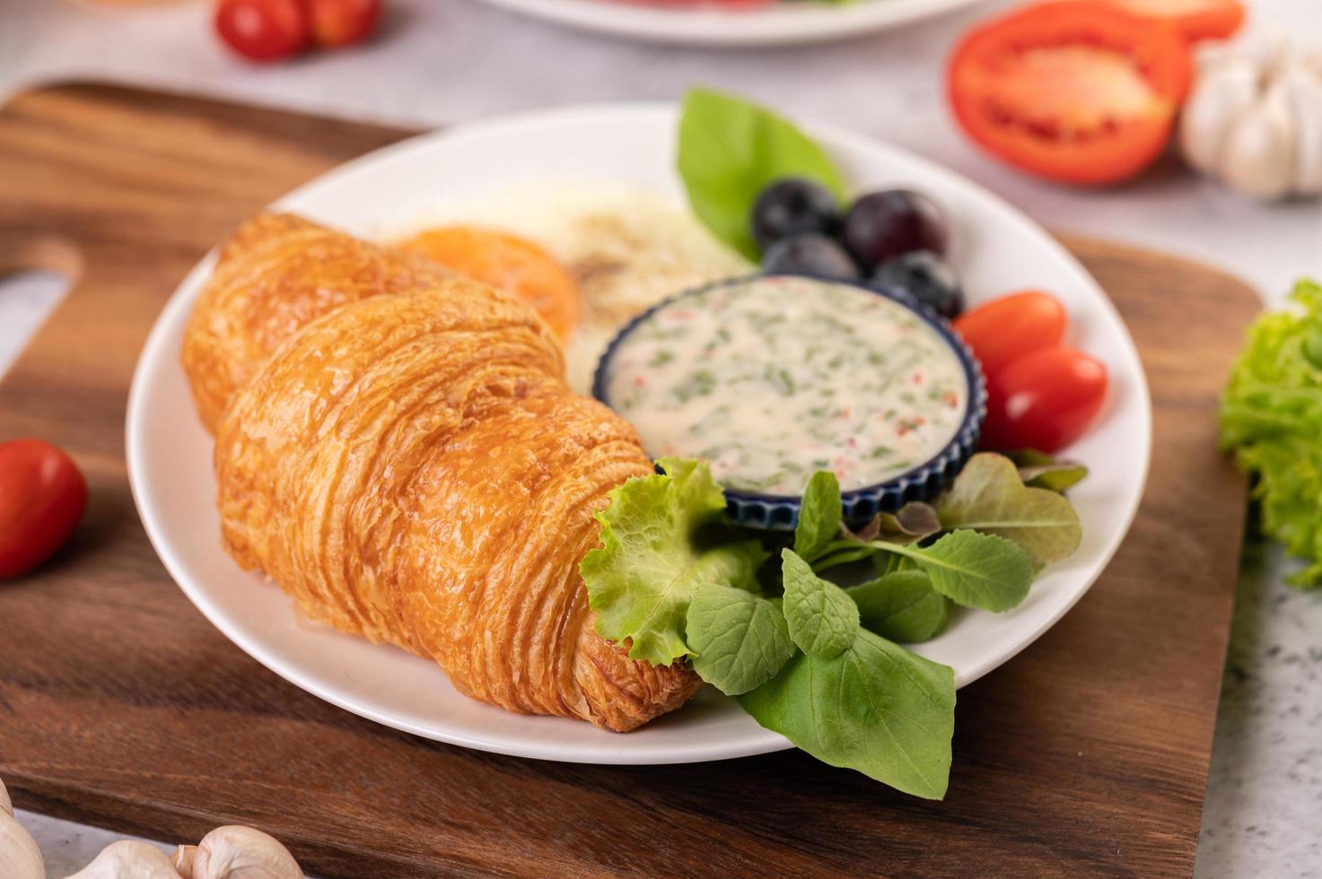 croissant, ovo frito, molho para salada, uvas pretas e tomates foto