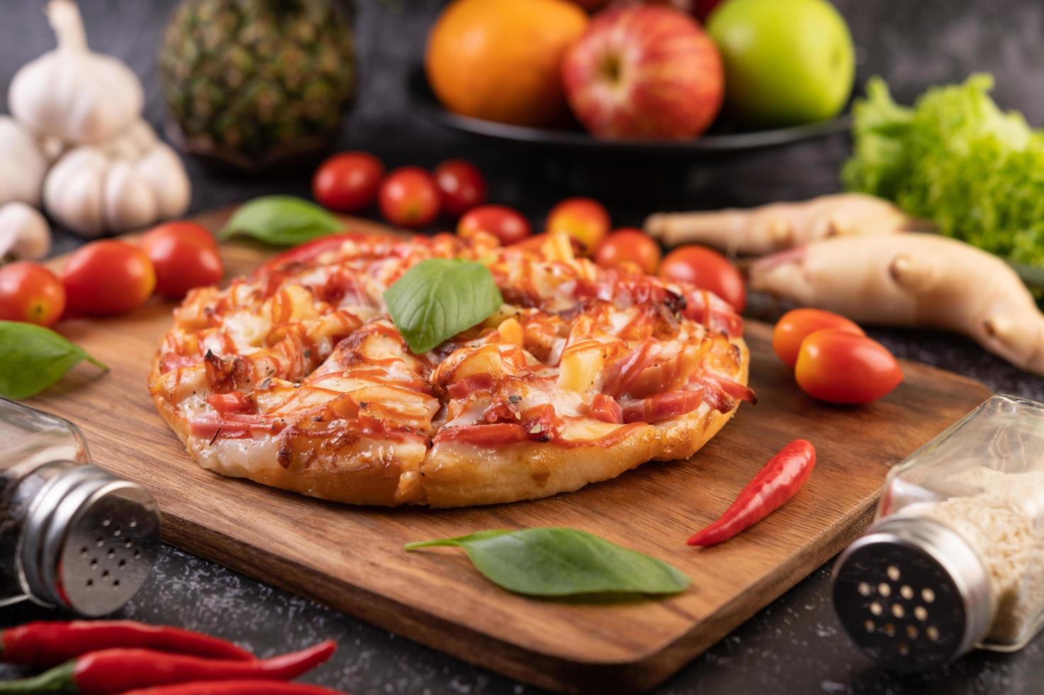 pizza caseira em bandeja de madeira com tomate, pimenta e manjericão foto