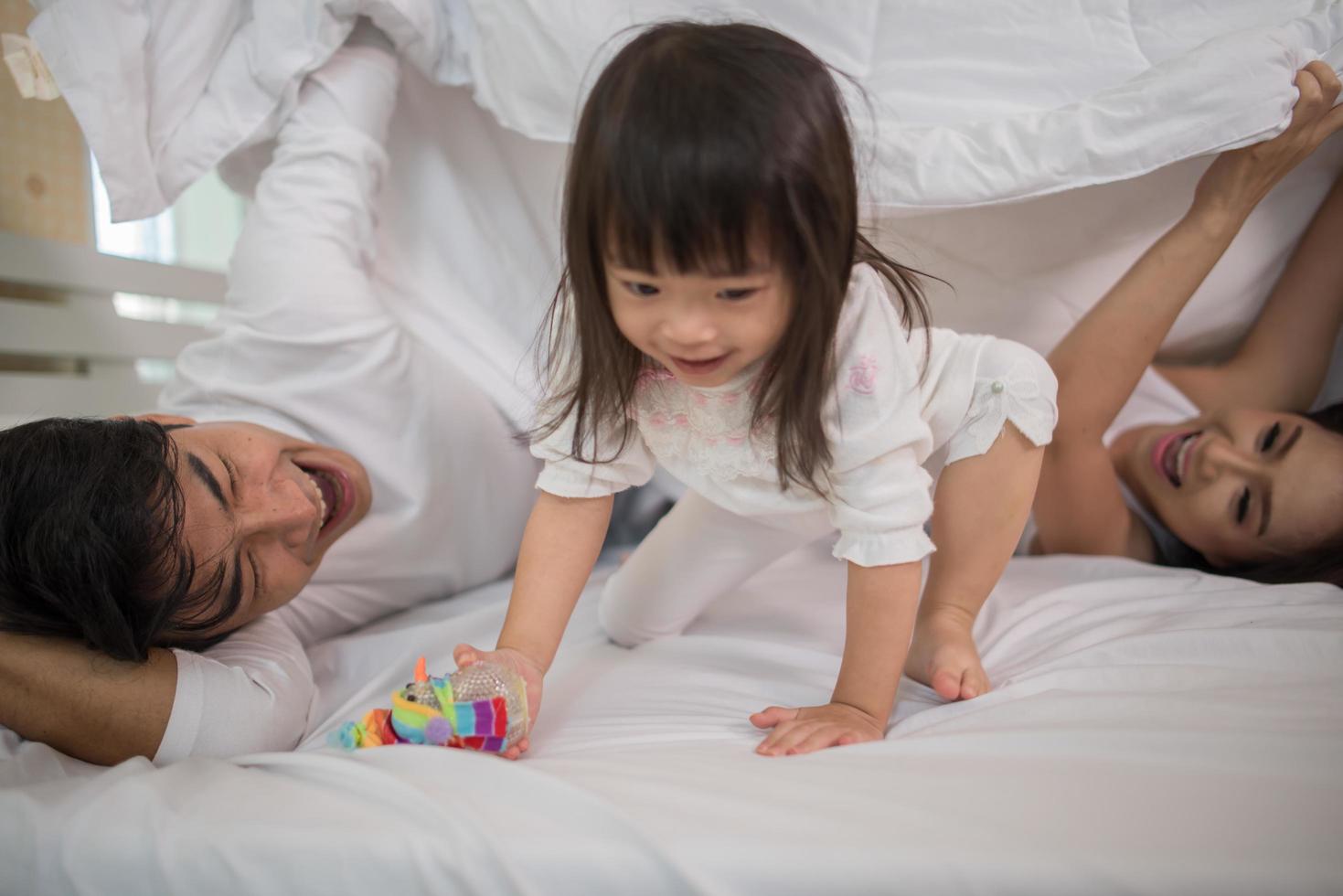 criança feliz com pais brincando na cama foto