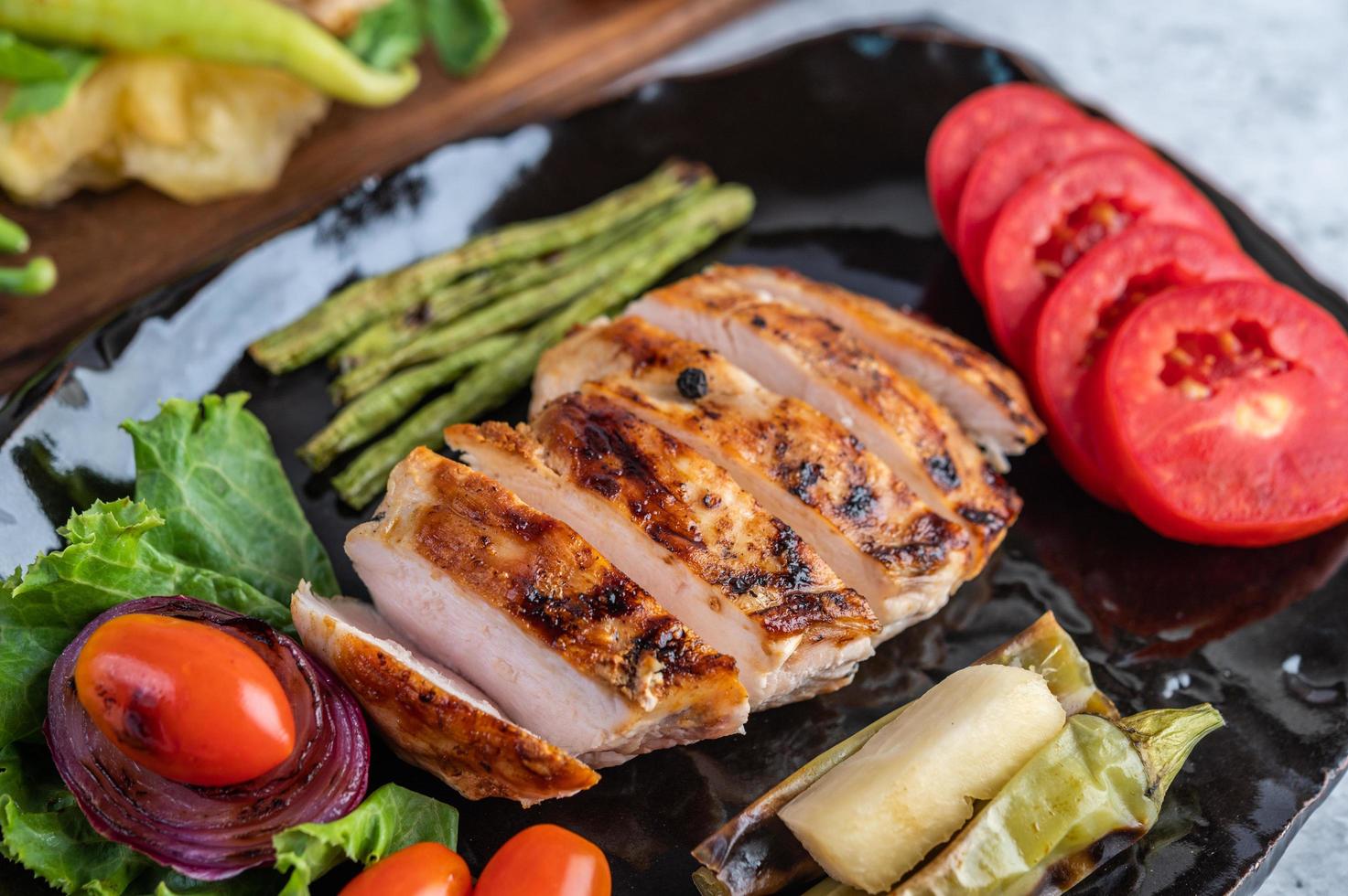 bife de frango com salada de legumes em um prato preto foto