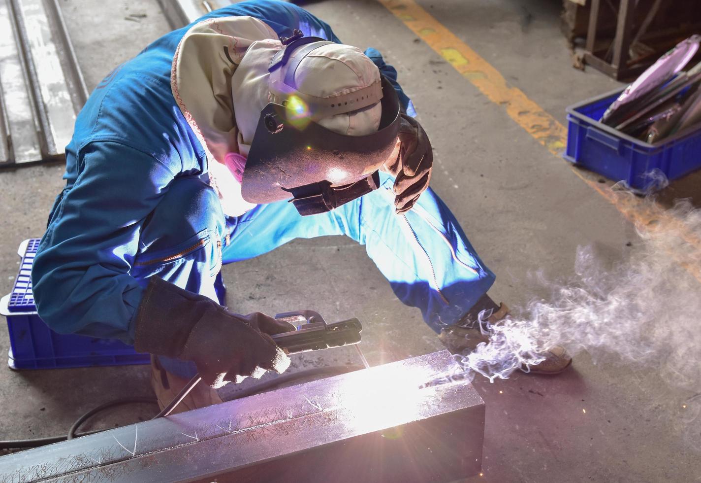 soldador de uniforme azul soldando a peça de trabalho foto