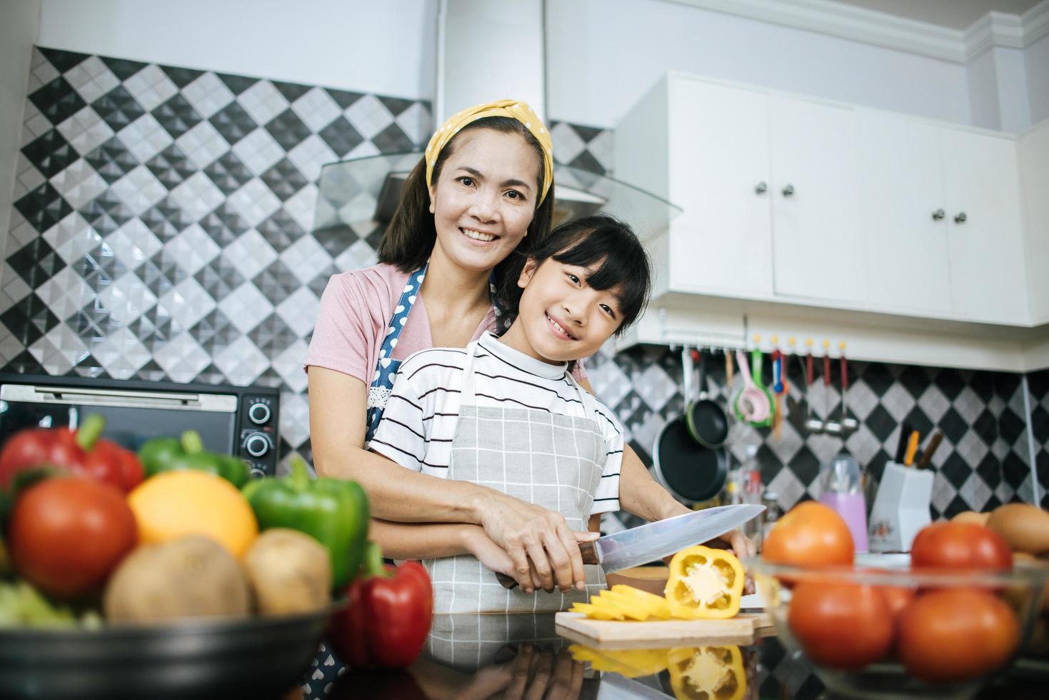 feliz mãe e filha preparando e picando vegetais na cozinha foto