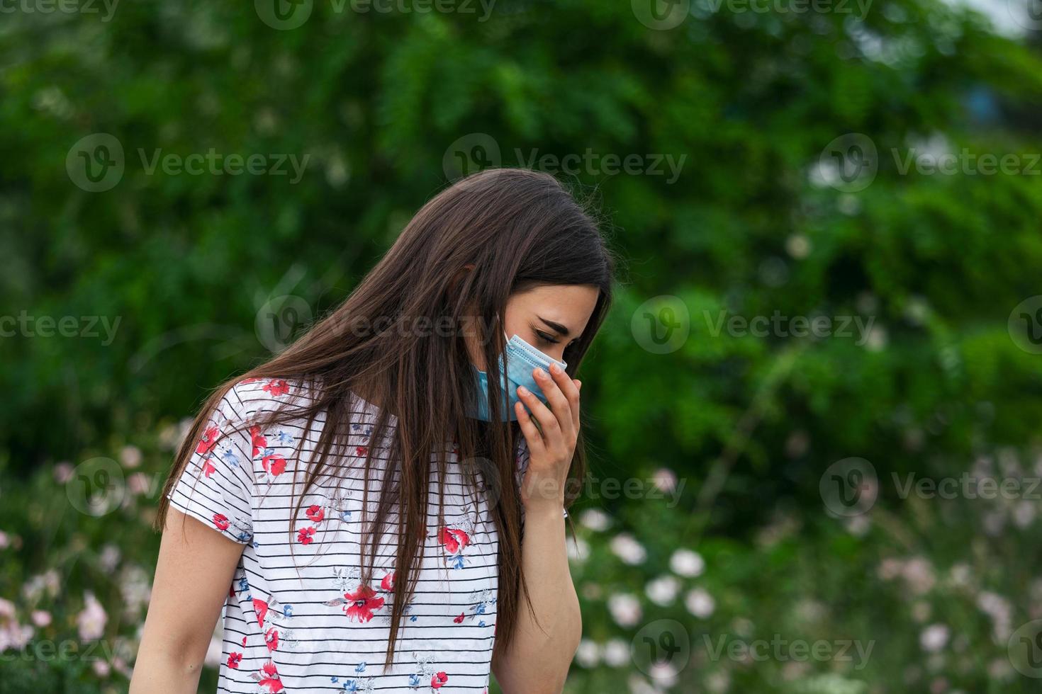 retrato de uma linda mulher triste em máscara médica espirra entre flores brancas. pandemia do coronavírus. conceito de não propagação do vírus. foto