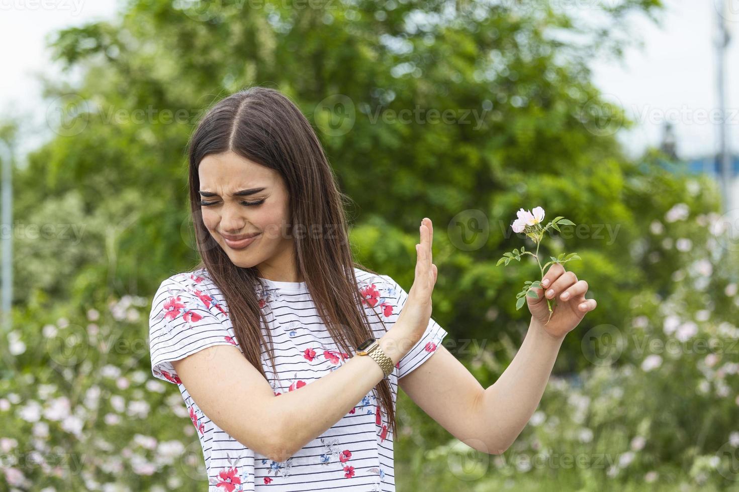 jovem com alergia ao pólen segurando uma flor e dizendo não... jovem com alergia ao pólen e grama. árvores floridas no fundo. primavera alergias sazonais e problemas de saúde. foto