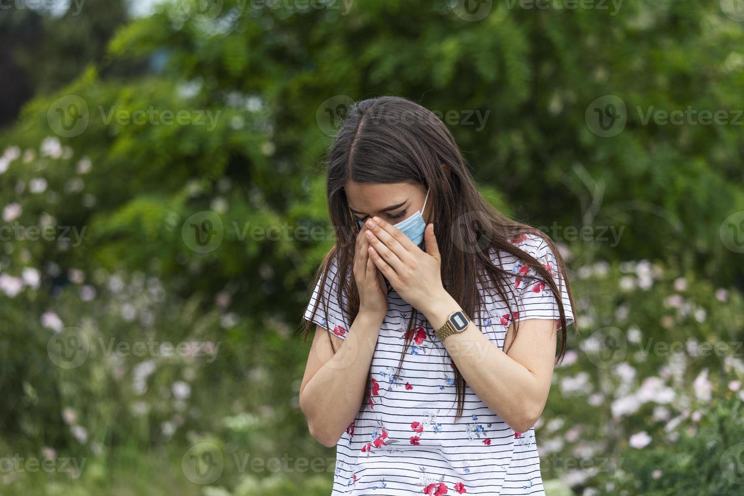 retrato de uma linda mulher triste em máscara médica espirra entre flores brancas. pandemia do coronavírus. conceito de não propagação do vírus. foto