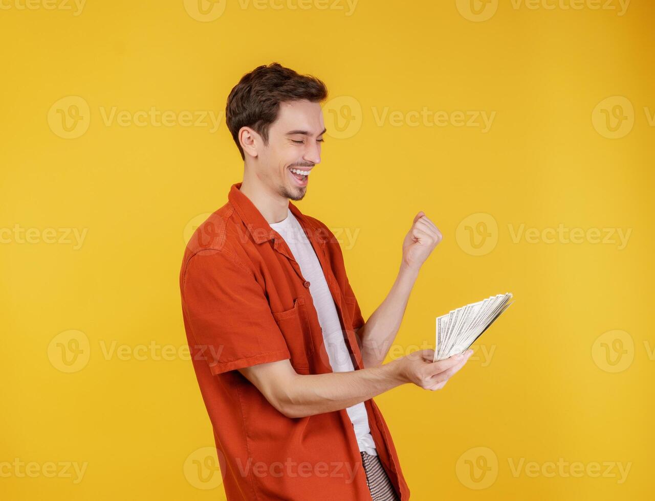retrato de um homem alegre segurando notas de dólar e fazendo gesto de vencedor cerrando o punho sobre fundo amarelo foto